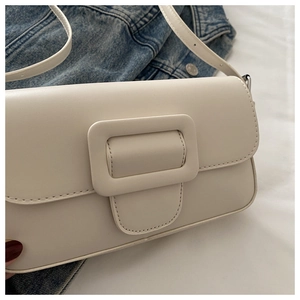 Detail of a creamy white flap bag with a square buckle on a denim jacket background