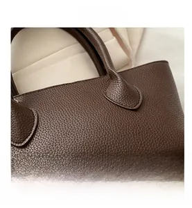 Detail of dark brown bucket bag showing pebble grain leather texture and handle stitching