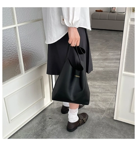 Detail of minimalist black matte leather tote bag with gold lettering shown on model