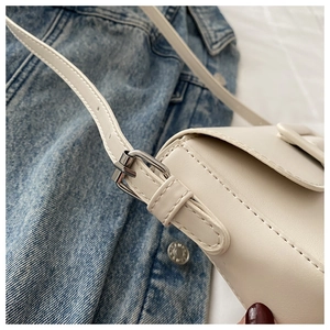 Detail of cream leather shoulder bag strap with silver buckle on blue denim background
