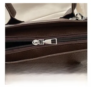 Detail view of smooth silver metal zipper and dark brown litchi pattern leather bag