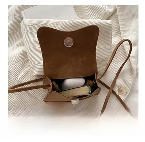 Detail view of brown suede crossbody bag showing interior storage for earbuds and lipstick