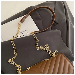 Detail of brown chevron quilted crossbody bag with gold chain strap on grey blazer
