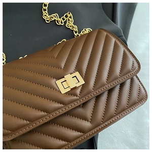 Detail of brown quilted faux leather bag with V-shaped texture and gold twist lock