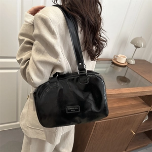 Minimalist black glossy tote bag with silver hardware on model in a cozy home setting