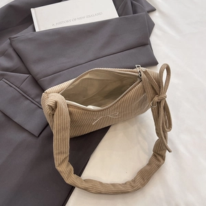 Beige corduroy shoulder bag featuring a large bow on the pleated strap and zip closure