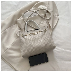 Détail du sac à main tissé beige avec chaîne dorée à nœuds et poignées cylindriques