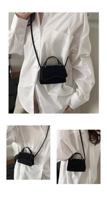 Detail of a black minimalist mini crossbody bag with a curved handle and slim shoulder strap