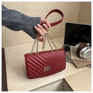 Macro view of burgundy V-quilted faux leather crossbody bag with gold chain strap detail