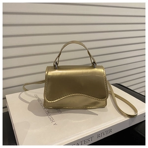 Close-up of gold mini handbag with wavy edge and glossy mirror finish on white books