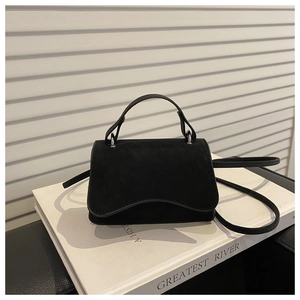Detail of minimalist black crossbody bag with wave flap design on white books
