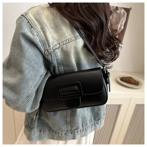 Detail view of a black flap shoulder bag with large square buckle on a model in casual wear
