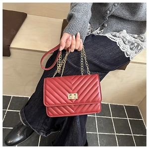 Detail of red quilted crossbody bag with gold chain strap and metallic twist lock