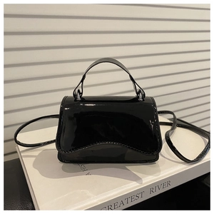 Detail of a black glossy patent leather mini bag on a white book with a top handle and strap