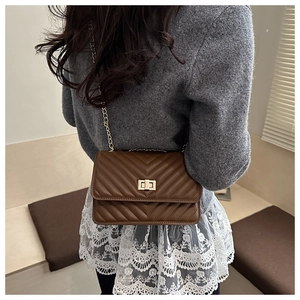 Close-up of brown quilted leather flap bag with gold chain strap worn by a model