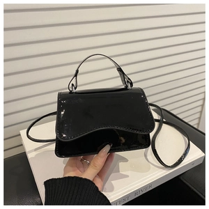 Detail of glossy black patent leather small square bag with round edges and handle