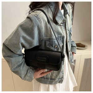 Detail of a black rectangular underarm baguette bag worn over a denim jacket