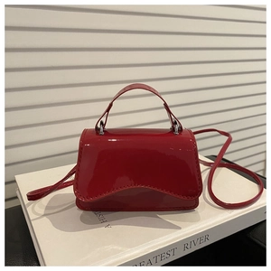 Detail of red patent leather mini bag with wavy flap design on white background