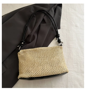Detailed view of woven straw bag with black leather strap and metal ring accent
