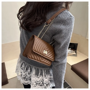 Brown quilted crossbody bag with V-shaped texture and gold twist-lock on a model