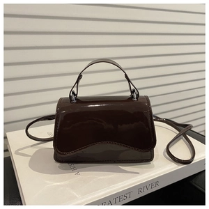 Detail view of mini dark chocolate crossbody bag with glossy patent finish on books
