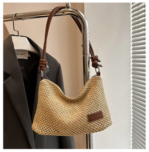 Detailed view of woven straw tote bag featuring brown leather strap and brand patch