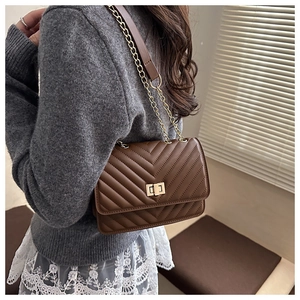 Detail of dark brown quilted crossbody bag featuring V-shaped stitching and gold chain