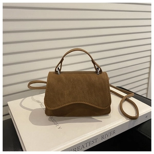 Close-up of brown matte leather handbag with silver hardware on a white book