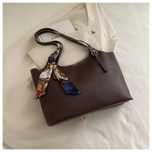 Detail of dark brown tote bag with printed silk scarf and golden buckle on leather handle