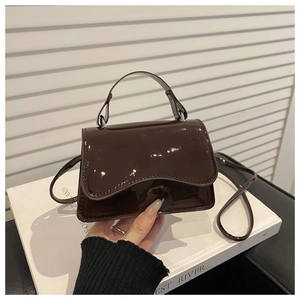 Detail of dark brown glossy patent leather mini crossbody bag with a curved handle