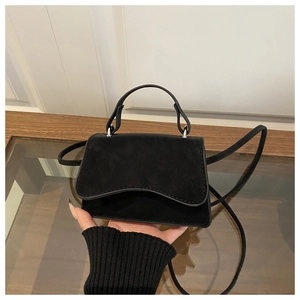 Detail of a minimalist black suede crossbody bag with silver hardware and top handle