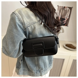 Detail of a black leather baguette bag with large square buckle worn by a model