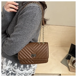Brown quilted chain bag with gold turn-lock closure shown in a lifestyle office setting