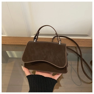 Detail of vintage brown leather mini crossbody bag with curved flap and silver hardware