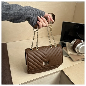 Detail view of brown quilted crossbody bag with V-stitch and gold chain strap in city setting