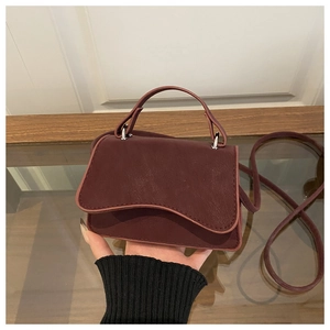 Close-up of burgundy leather crossbody bag with wave design flap and silver hardware