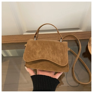 Macro detail of brown textured leather crossbody bag with wavy flap and round handle