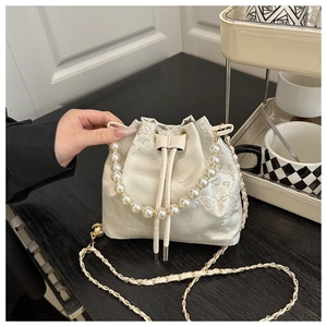 Detail of embroidered satin bucket bag featuring pearl handle and golden chain strap