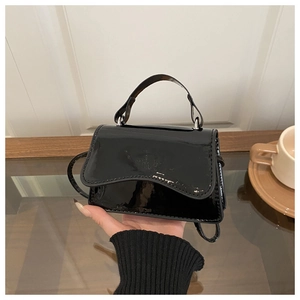 Close-up of black glossy patent leather mini handbag with wavy flap and round handle