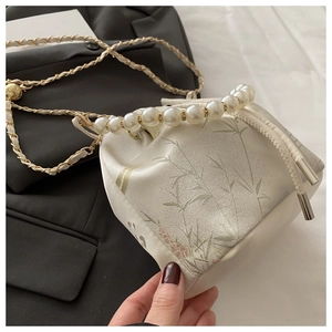 Detail of satin bucket bag featuring pearl handle and embroidered bamboo leaf patterns