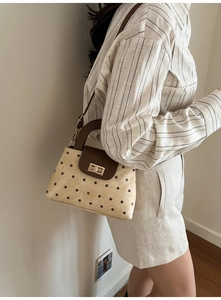 Gros plan d'un sac à pois beige avec fermoir doré porté par un mannequin