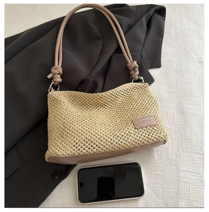Beige woven straw tote with brown leather straps and metal logo shown with a smartphone