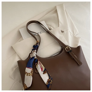 Close-up of vintage brown leather tote with white stitching and decorative silk scarf
