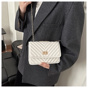 Close-up of white embossed crossbody bag with gold chain strap on a grey blazer
