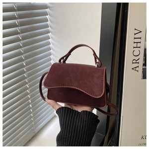 Detail of burgundy leather handbag showing asymmetric wave flap and litchi texture