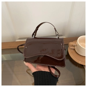 Detail of a chocolate brown patent leather handbag with silver hardware and top handle