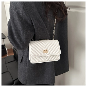 Detailed view of white quilted crossbody bag with gold turn-lock and chain strap on model