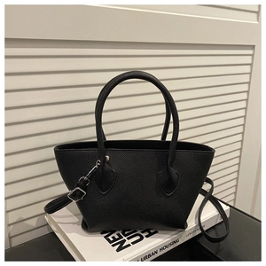Close-up of black bucket bag with lychee grain texture on white book background