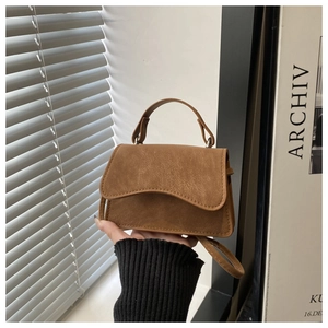 Detail of retro brown suede bag with unique wave-shaped flap and textured finish