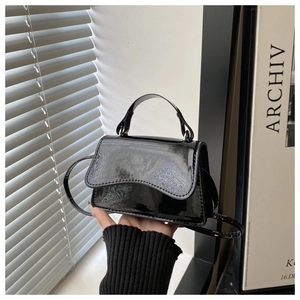 Detail of black patent leather mini bag featuring wavy flap edges and glossy finish